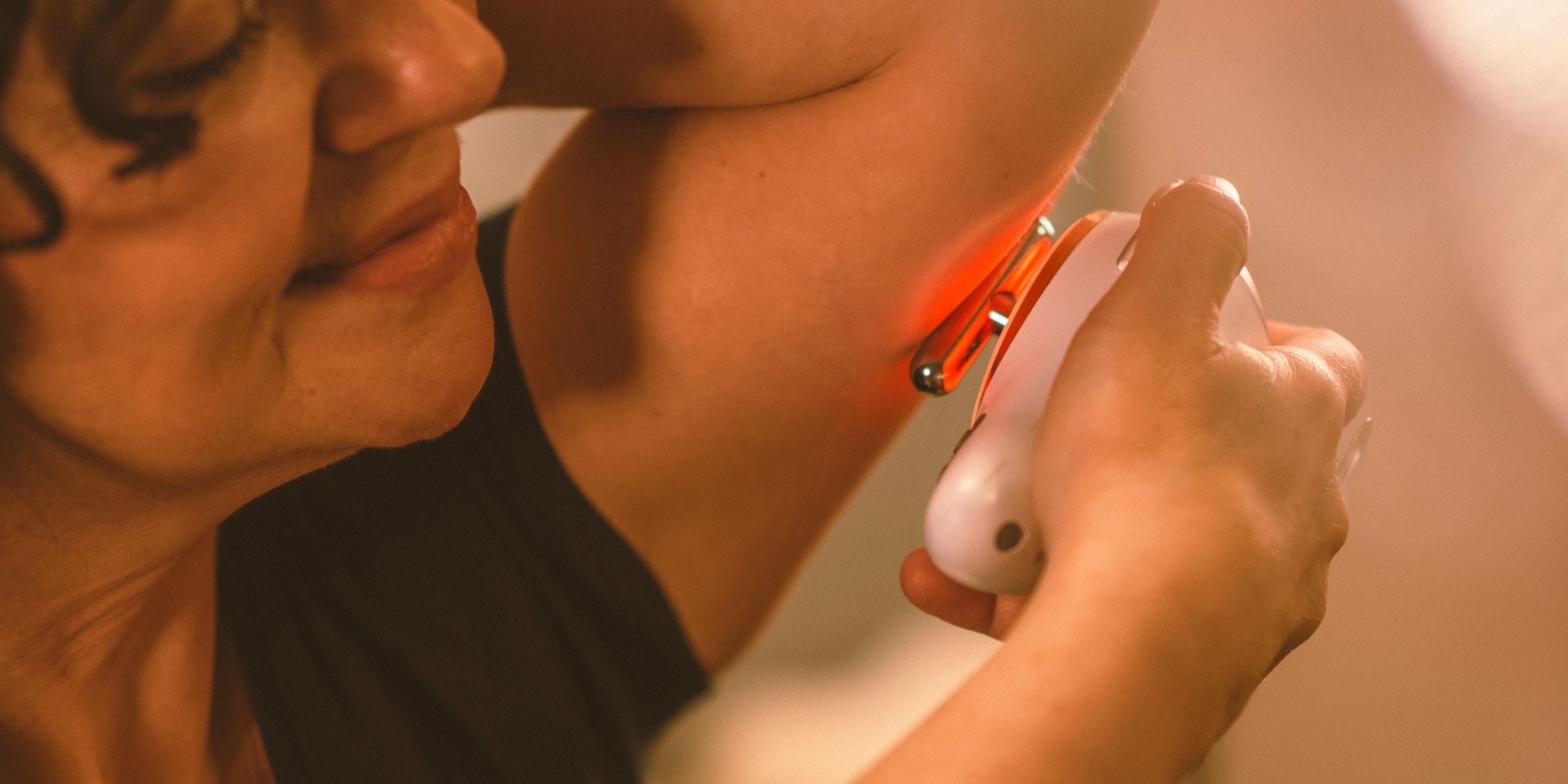 Frau hält sich Evosonics SoundWave Personal an den Oberarm um eine Lymphdrainage gegen schlaffe Oberarme mit Schallvibrationen und Rotlicht  durchzuführen. | Therapiegold